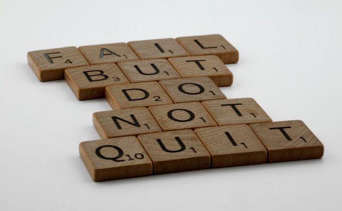 Wooden Scrabble tiles arranged to spell 'Fail but do not quit,' inspiring determination.