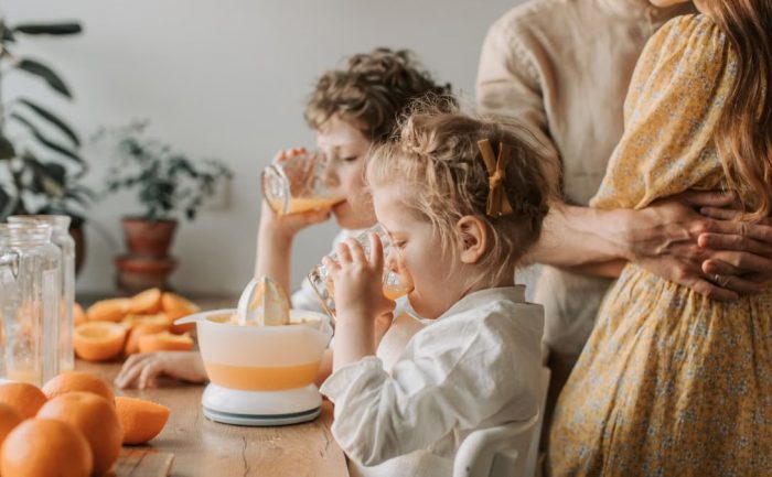 A loving family moment with children drinking fresh orange juice indoors.